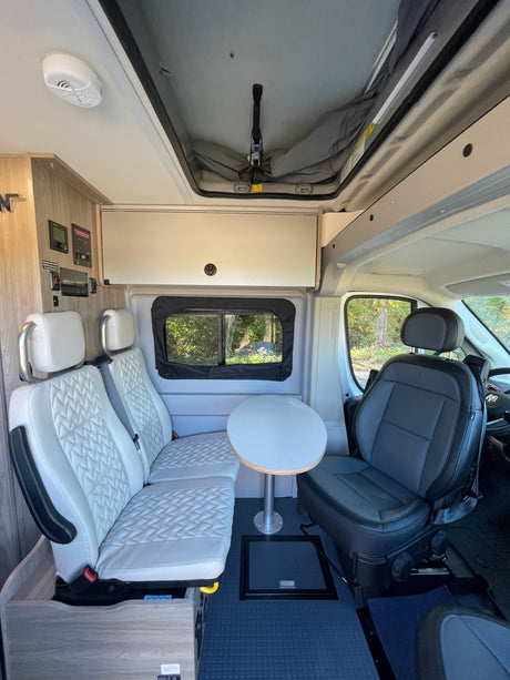 Spacious RV rental interior with quilted seats, table, control panel, and pop-top roof, ready for travel.