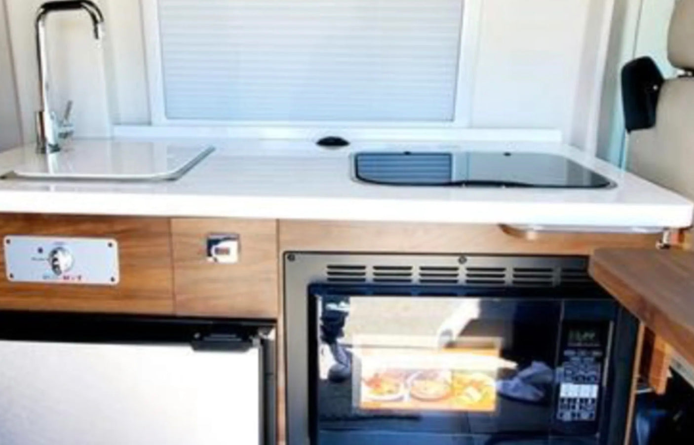 Compact RV rental kitchen featuring a sink, cooktop, microwave, and under-counter refrigerator for convenient travel.