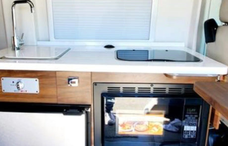 Compact RV rental kitchen featuring a sink, cooktop, microwave, and under-counter refrigerator for convenient travel.
