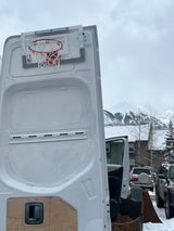 RV rental with a mini basketball hoop mounted on the rear door, parked in snowy mountains. Perfect for winter fun!