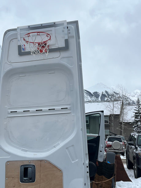 RV rental with a mini basketball hoop mounted on the rear door, parked in snowy mountains. Perfect for winter fun!