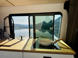 Modern rv rental kitchen with a large window revealing a serene lake and majestic mountains. Pan on induction cooktop.