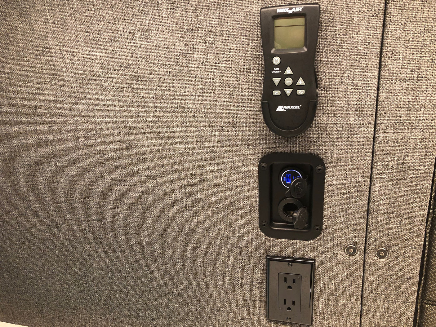 RV rental interior: A Maxxair remote, USB/12V charging ports, and a standard outlet on a textured gray wall.
