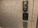 RV rental interior: A Maxxair remote, USB/12V charging ports, and a standard outlet on a textured gray wall.