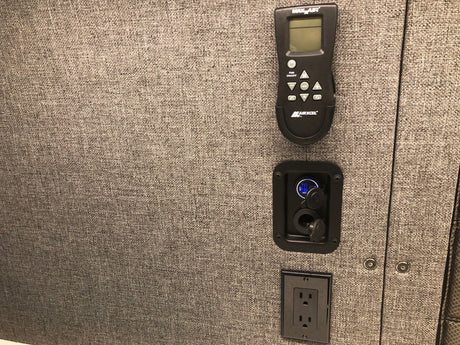 RV rental interior: A Maxxair remote, USB/12V charging ports, and a standard outlet on a textured gray wall.