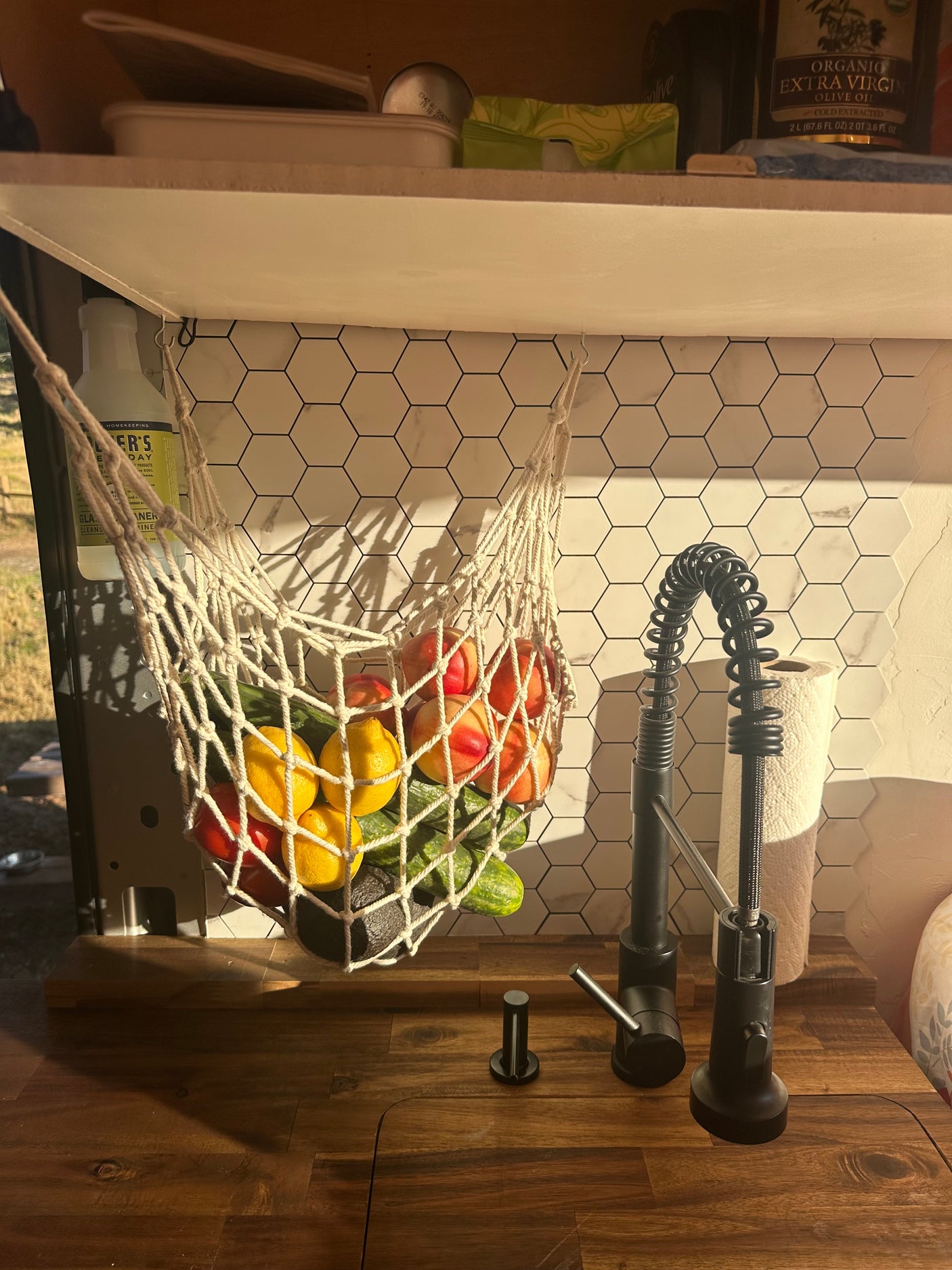 An RV rental's well-organized kitchen: fresh produce in a hanging net, sleek black faucet, and hexagon tile backsplash.