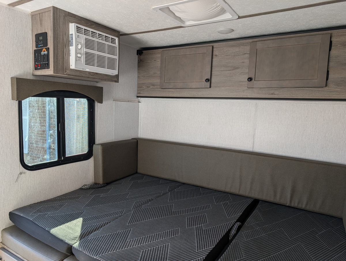 RV rental interior featuring a convertible bed/dinette with patterned cushions, overhead AC, control panel, and cabinets. — photo 10
