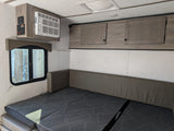 RV rental interior featuring a convertible bed/dinette with patterned cushions, overhead AC, control panel, and cabinets.