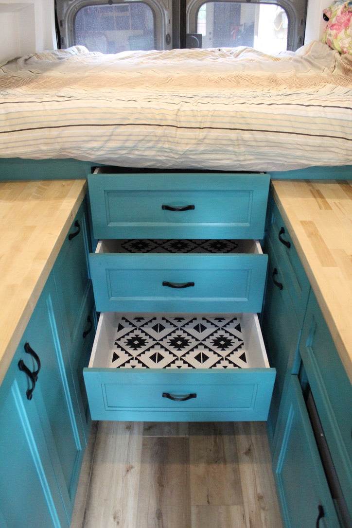 Explore an RV rental's custom storage! Teal cabinets & drawers with patterned liners under a comfy bed.
