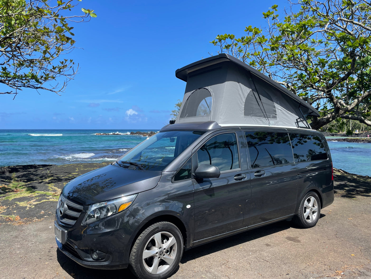 Dark grey pop-top camper van rv rental by Hawaii's coast. Enjoy scenic ocean views & nature adventures.
