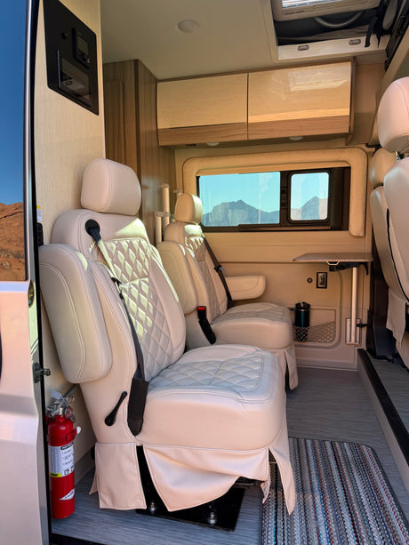 Inside a luxurious RV rental, cream captain's chairs offer comfort with mountain views, modern controls, and safety gear visible.