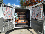 Cozy camper van interior, possibly an RV rental, featuring Route 66 curtains, custom shelving, and a "home sweet home" mat.