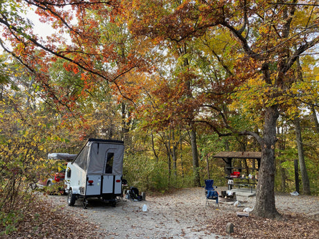 Enjoying an RV rental at a scenic autumn campsite. A pop-up camper, vehicle, and picnic area are nestled among colorful fall trees.