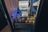 RV rental fridge stocked with beverages like kombucha & cocktails, open to a scenic ocean view.