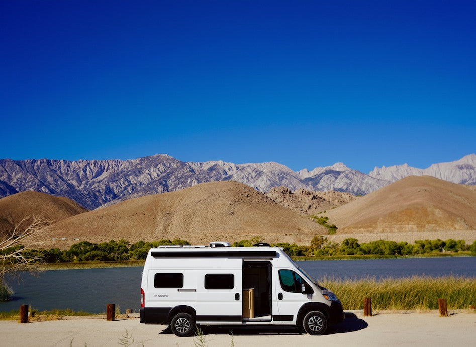 Scenic rv rental parked by a lake with majestic mountains under a clear blue sky, perfect for outdoor adventures.