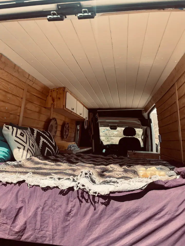 Inside a spacious RV rental: a comfy bed with patterned blankets, wood-paneled walls, and white ceiling in a camper van. — photo 10