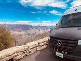 Mercedes-Benz Sprinter RV rental at Grand Canyon scenic point. Blue sky, vast landscape views.