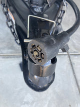 Close-up of a 7-pin trailer connector for an RV rental, showing exposed pins, hitch, and safety chains.