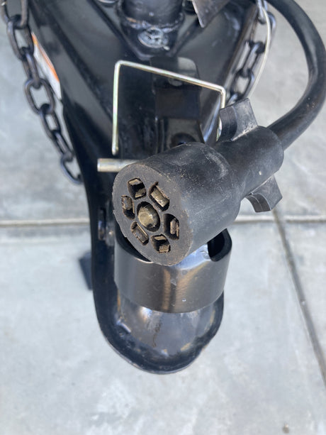 Close-up of a 7-pin trailer connector for an RV rental, showing exposed pins, hitch, and safety chains.
