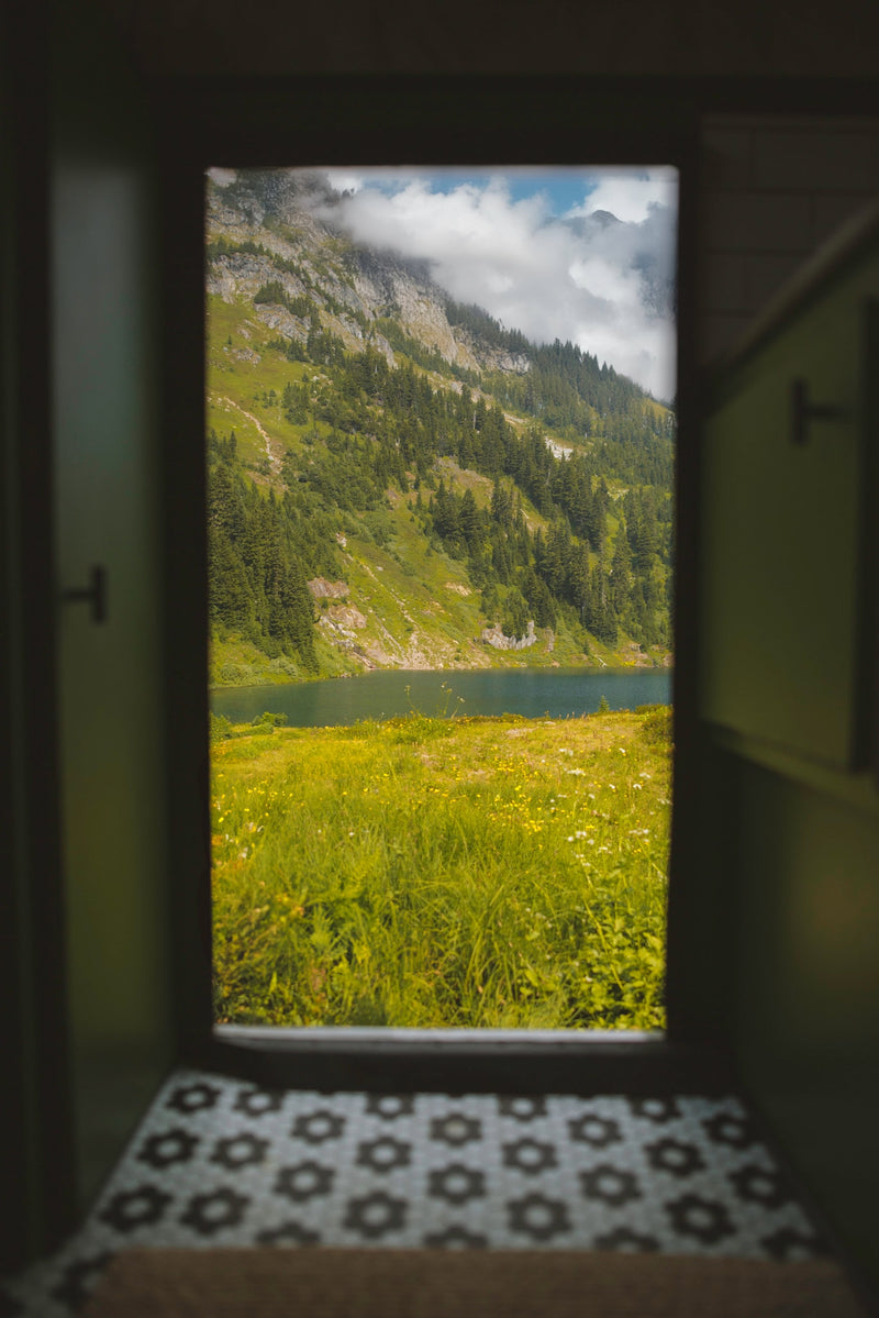 Escape with an RV rental! Gaze out the door at a vibrant mountain landscape with a serene lake, lush trees, and wildflowers. — photo 12