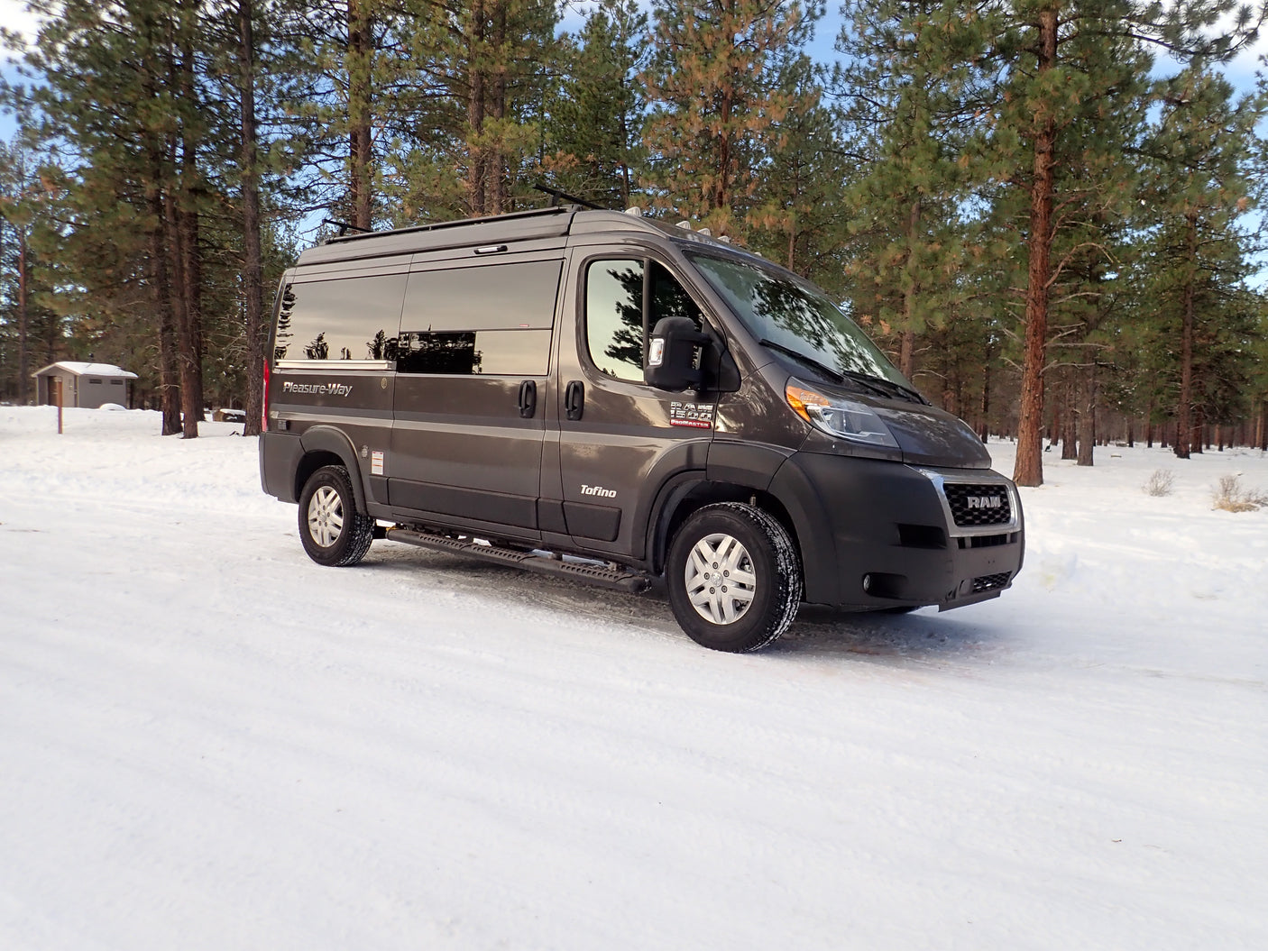 Gray camper van RV rental parked in a beautiful snowy pine forest, ready for winter adventure.