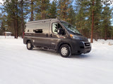 Gray camper van RV rental parked in a beautiful snowy pine forest, ready for winter adventure.