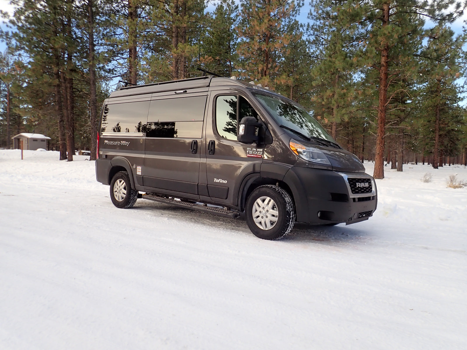 Gray camper van RV rental parked in a beautiful snowy pine forest, ready for winter adventure.