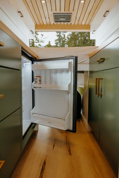 Inside this RV rental: an open mini-fridge, wood flooring, and olive green cabinets, perfect for mobile living.