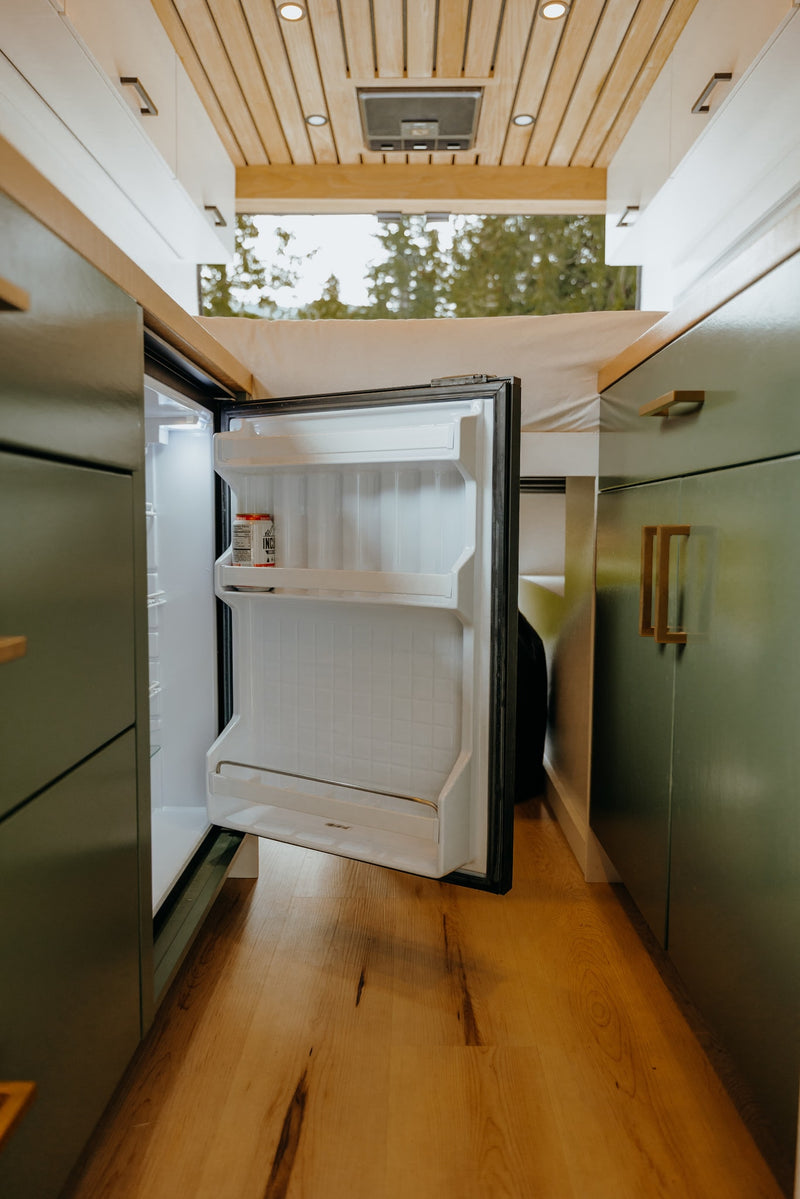 Inside this RV rental: an open mini-fridge, wood flooring, and olive green cabinets, perfect for mobile living. — photo 9