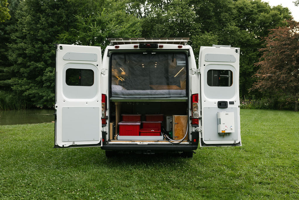 Rear of an RV rental camper van with open doors, showing a bed, storage, and external water heater, ready for travel. — photo 7