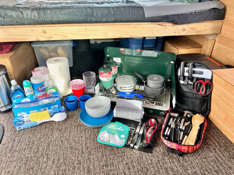 Organized rv rental camping kitchen setup: Coleman stove, pots, dishes, cleaning supplies & cooking tools ready for adventure.