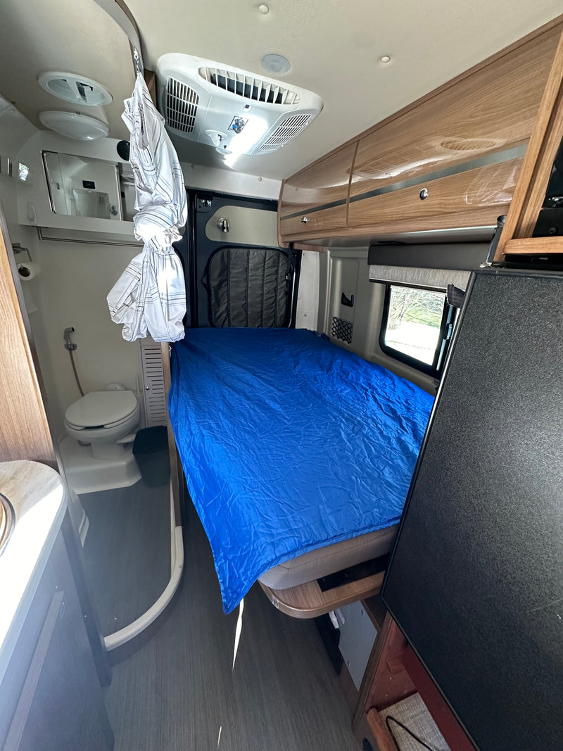 Compact rv rental interior with a blue bed, small bathroom, and overhead storage, ideal for mobile living. — photo 3