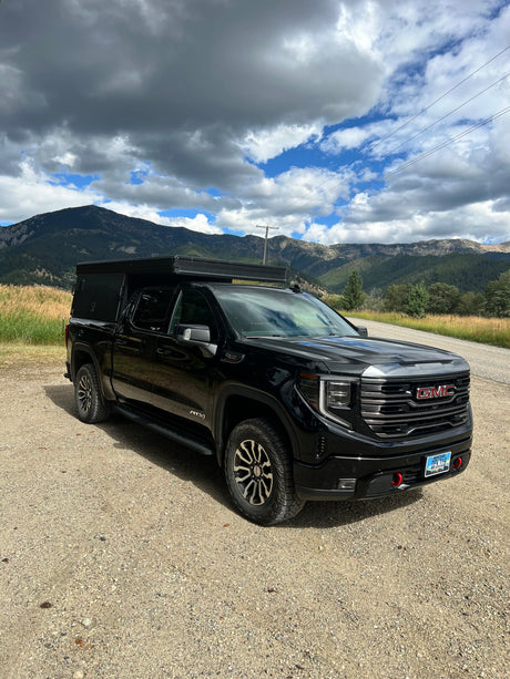 Explore Montana's mountains with this black GMC truck & camper, an ideal RV rental for off-grid adventures under a dynamic sky.