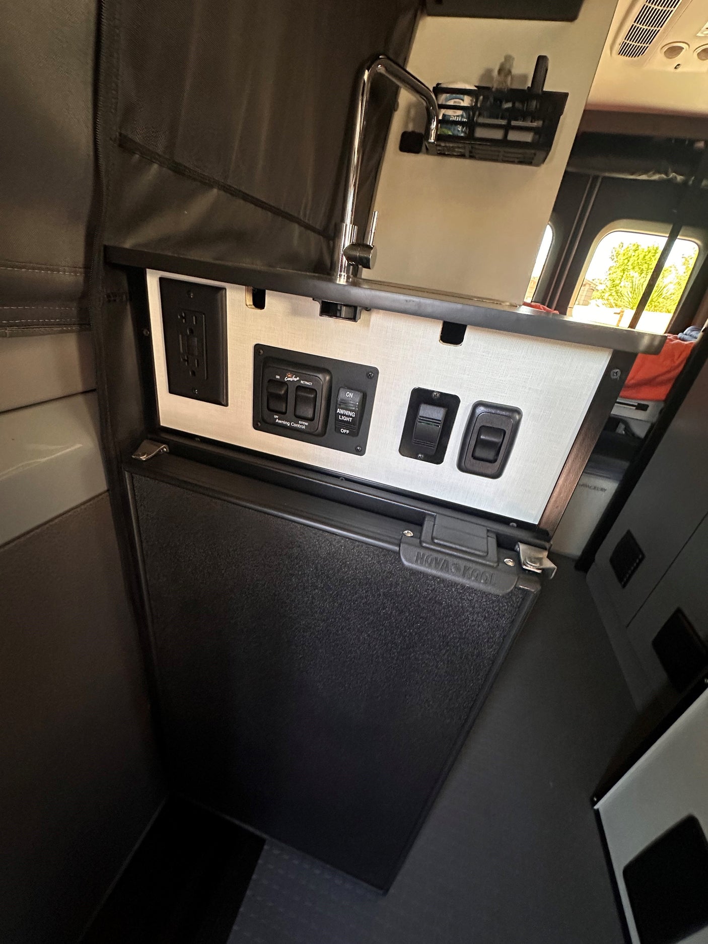 RV rental's compact kitchen area: Chrome faucet, Nova Kool fridge, power outlets, and awning controls are clearly visible.