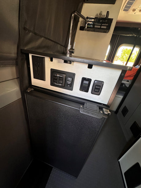 RV rental's compact kitchen area: Chrome faucet, Nova Kool fridge, power outlets, and awning controls are clearly visible.