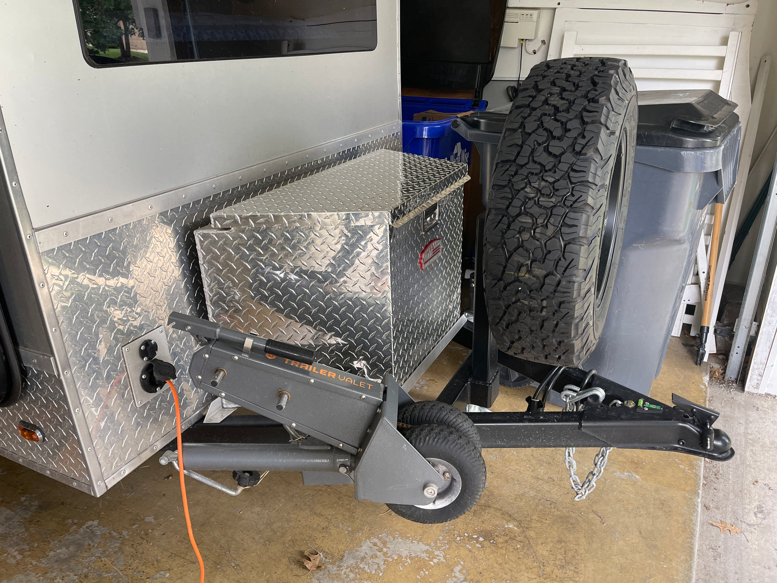 Front of a compact RV rental trailer, featuring a diamond plate storage box, spare tire, and a Trailer Valet mover.