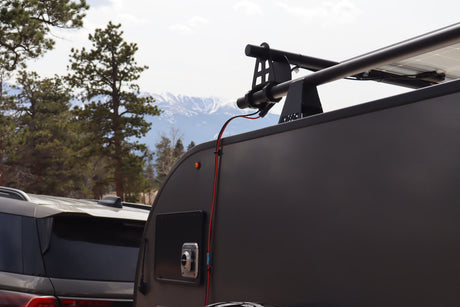 This rv rental shows a teardrop camper with solar panels, a roof rack, and an electrical hookup, set against scenic mountains.