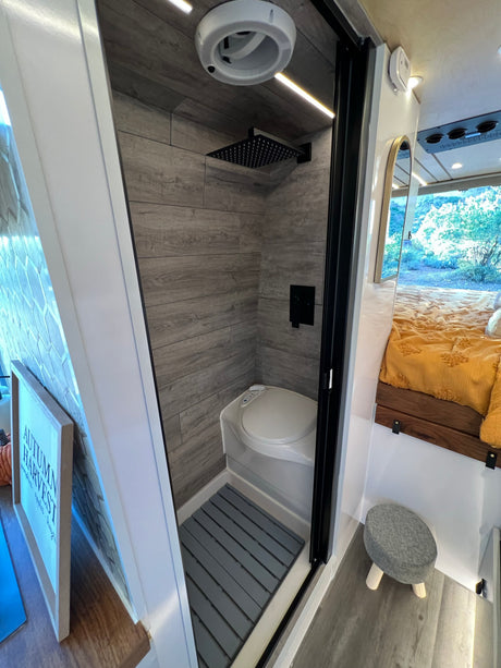 This RV rental showcases a compact interior: a modern shower-toilet wet bath, a cozy bed, and large window views.