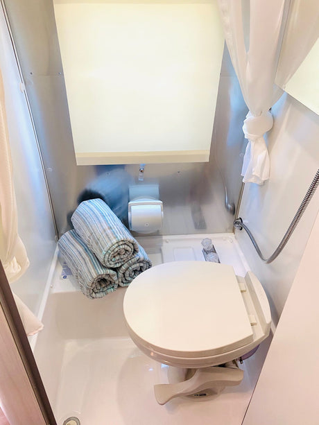 Experience a cozy RV rental bathroom featuring a toilet, compact shower, and clean, rolled towels for your trip.