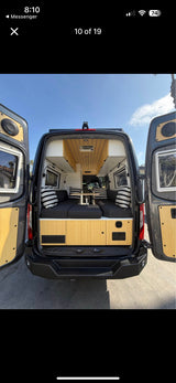 RV rental: Modern camper van interior with open back doors, featuring a seating/bed area, table, and wood accents.