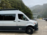 An Airstream RV rental parked at a scenic viewpoint, with a grand arched bridge and foggy evergreen forest in the background.