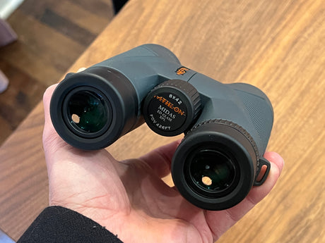 Gray Athlon Midas 8x42 binoculars held in hand, ideal for wildlife viewing on your next rv rental trip or nature exploration.