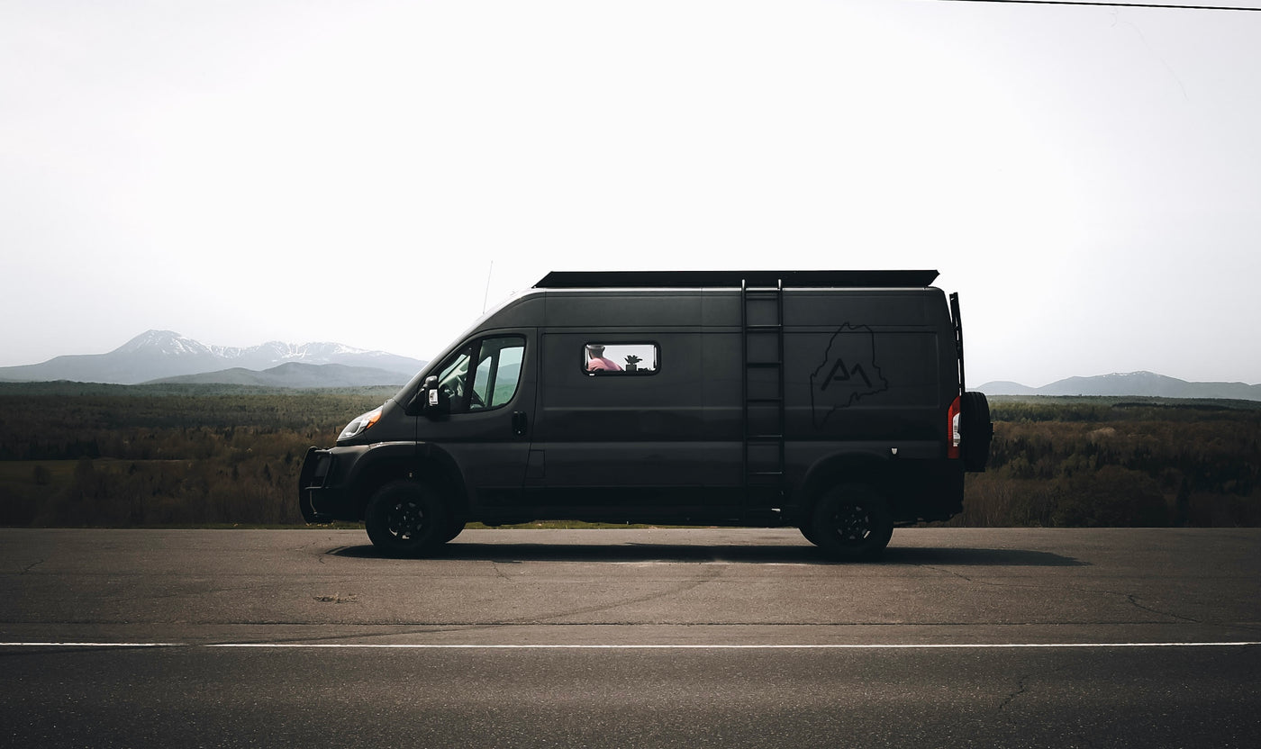 A sleek, dark RV rental van rests on a scenic mountain road, ready for adventure. Ideal for a memorable road trip.