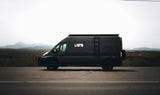 A sleek, dark RV rental van rests on a scenic mountain road, ready for adventure. Ideal for a memorable road trip.