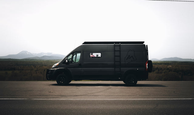 A sleek, dark RV rental van rests on a scenic mountain road, ready for adventure. Ideal for a memorable road trip.