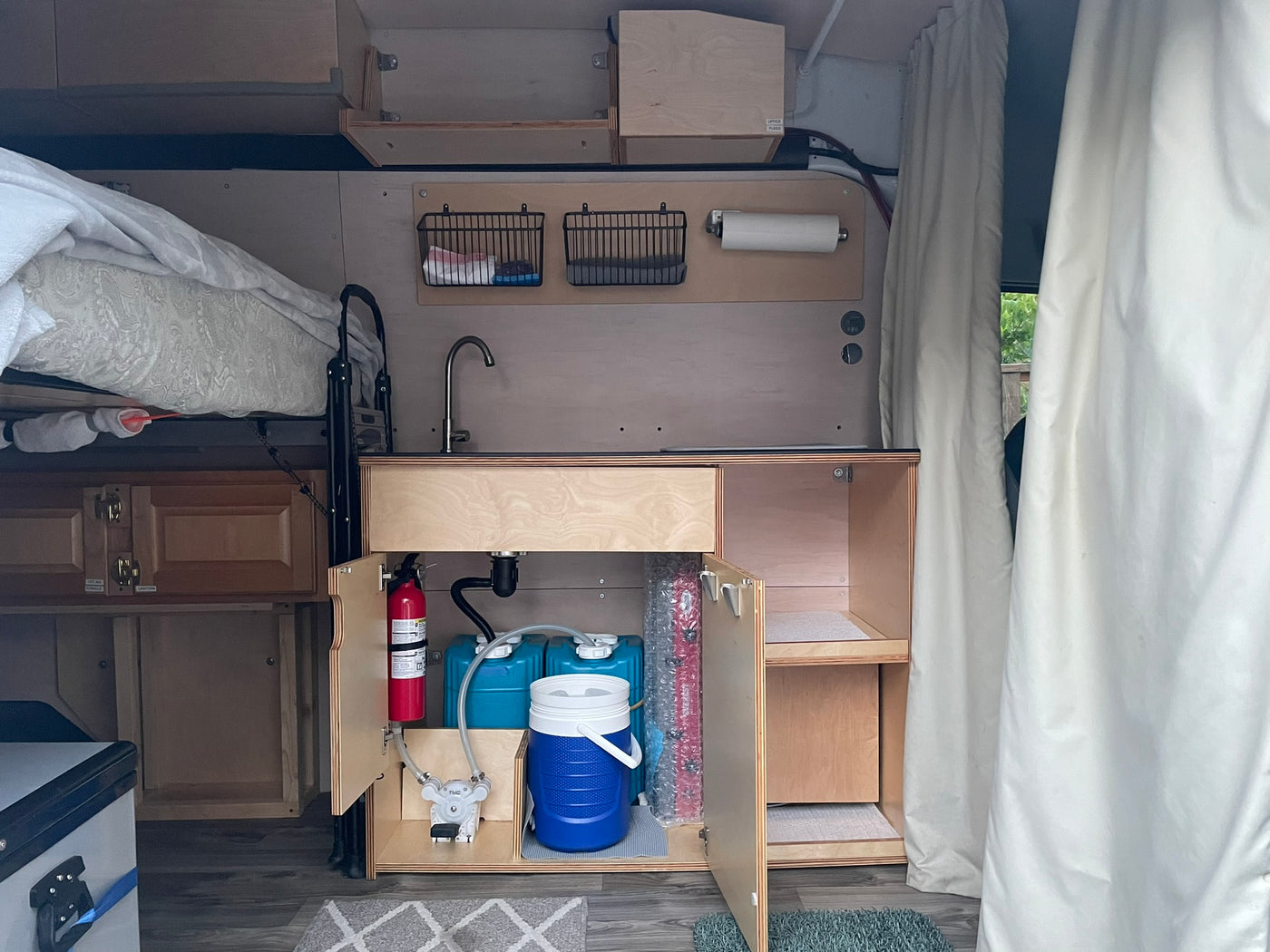 Compact RV rental interior: kitchenette with sink, water system, fire extinguisher, elevated bed, and organized storage for travel. — photo 10