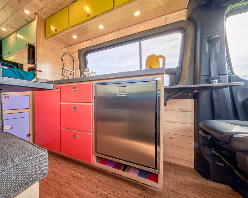Bright and functional RV rental interior with a compact kitchen, colorful cabinets, and a fold-down table. Perfect for van life adventures. — photo 13