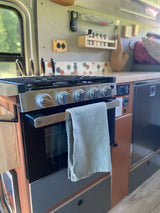 Modern RV rental kitchen featuring a GE Profile stove/oven, colorful backsplash, smart storage, and a compact fridge.