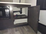 RV rental kitchen area with built-in microwave, sink, and open under-sink cabinet showing plumbing & shelf.