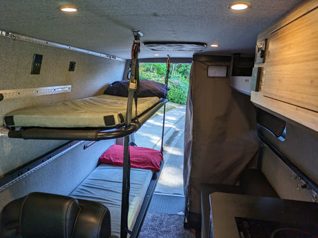Inside an rv rental, showing stacked bunk beds, a compact kitchen, and seating in a customized camper van.